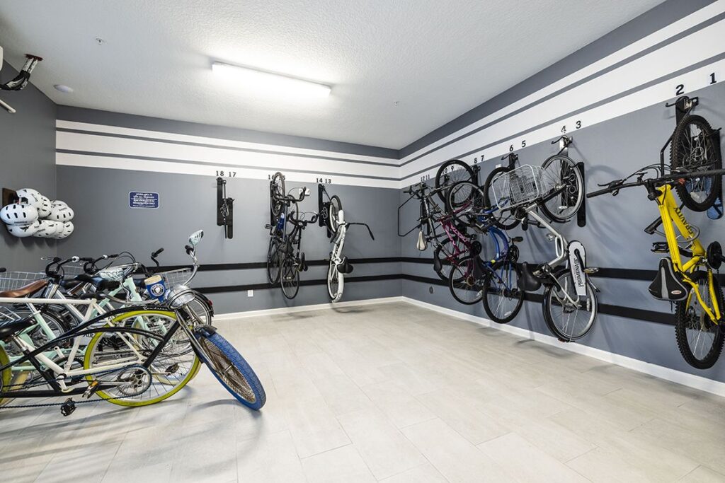 A bike storage room with bicycles securely mounted on racks attached to the walls. Helmets hang to the left. The room is well-lit and organized, with numbered spots for each bike.