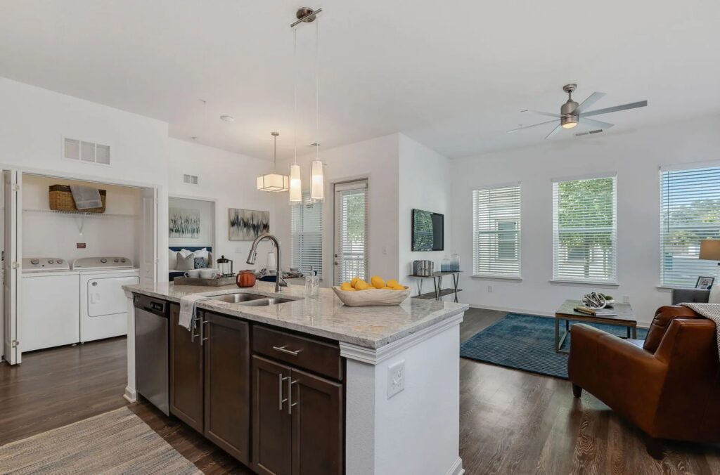 Modern open-concept living area with a kitchen island, stainless steel appliances, and a cozy living space. Washer and dryer are visible in a separate laundry nook.