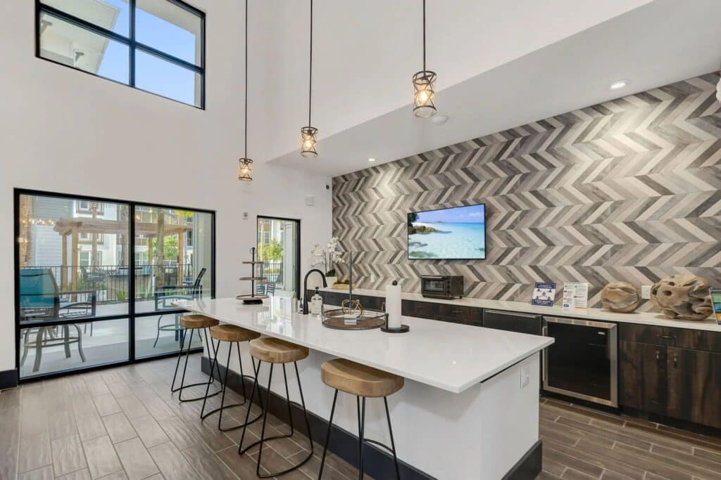 Modern kitchen with a chevron-patterned backsplash, white island with barstools, pendant lights, and large windows.