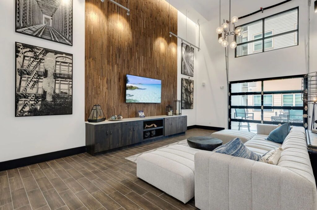 A modern living room with wooden accents features a large sectional sofa, a wall-mounted TV, black-and-white artwork, and industrial-style lighting.